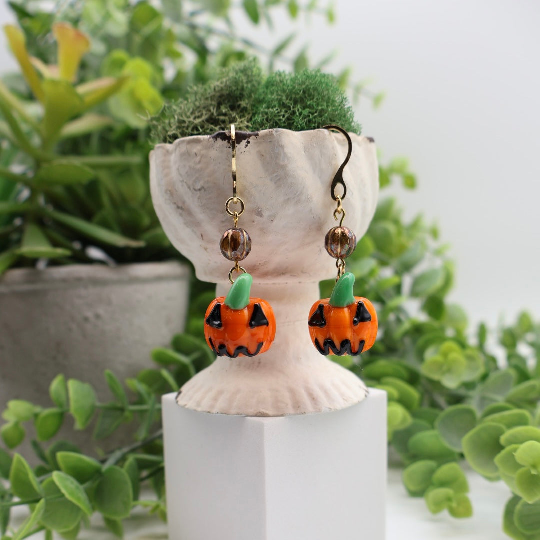 Pumpkin-shaped earrings on a white stand with green plants in the background