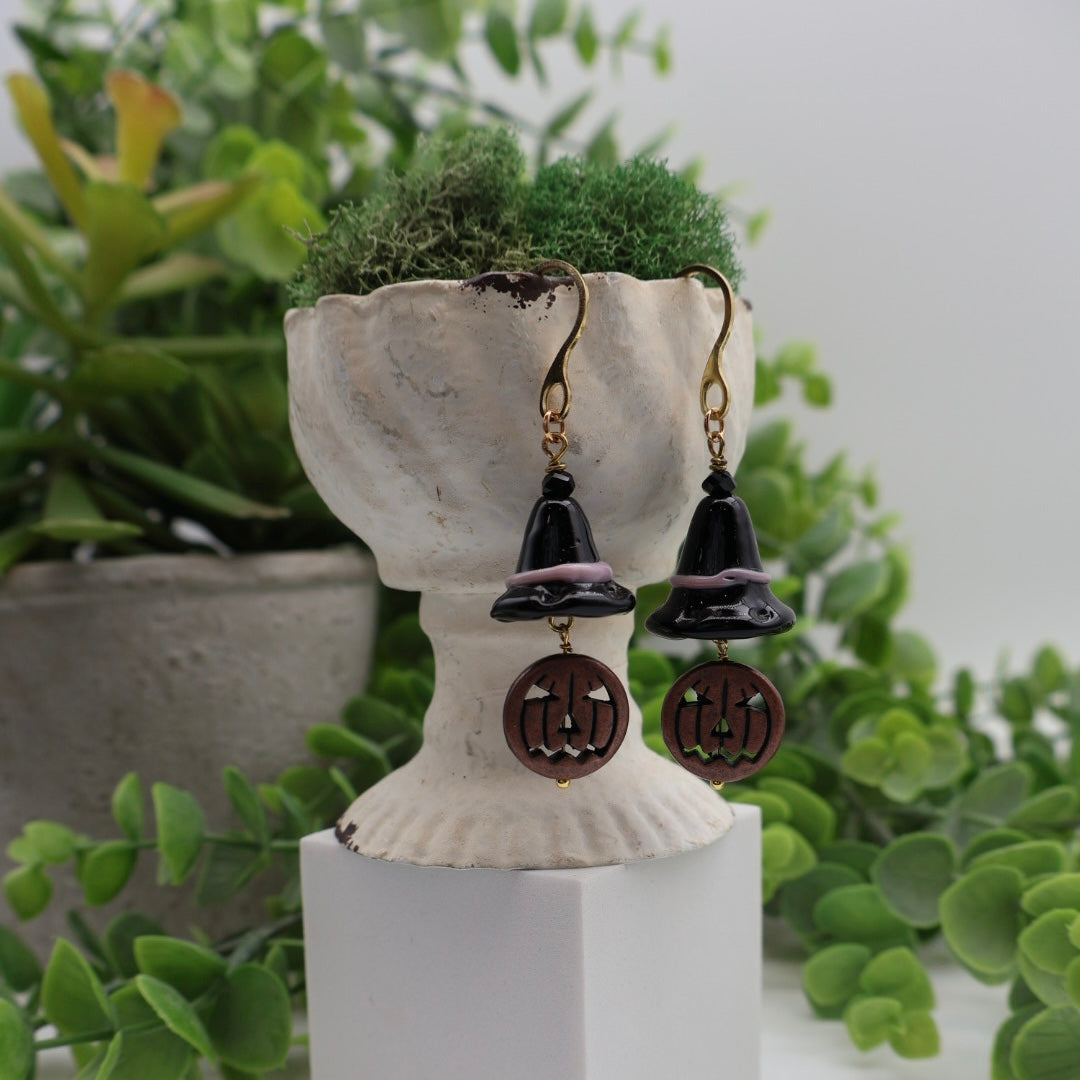 Pair of earrings on a decorative stand with green plants in the background