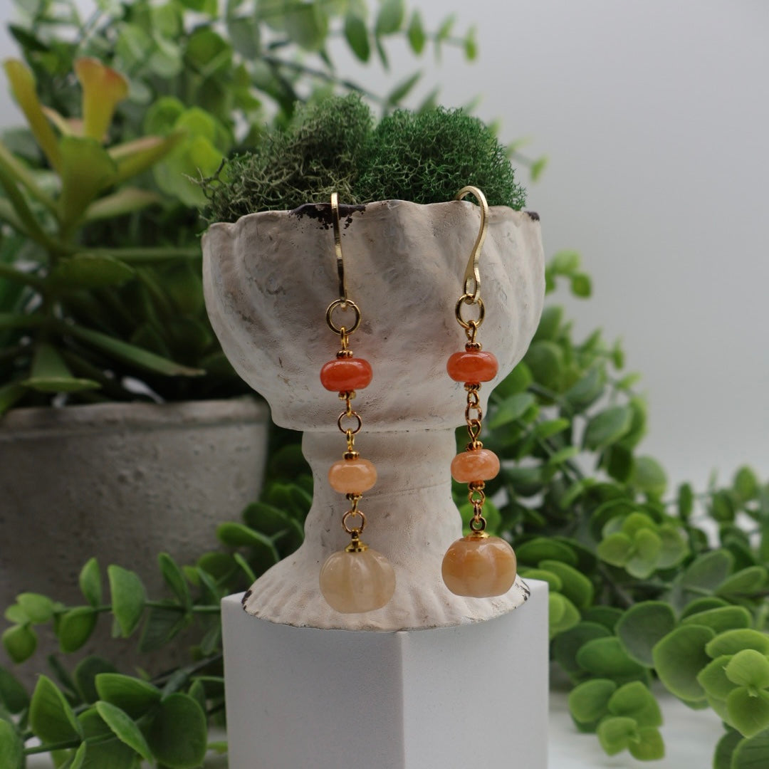 Pair of earrings with orange beads on a decorative stand with plants in the background