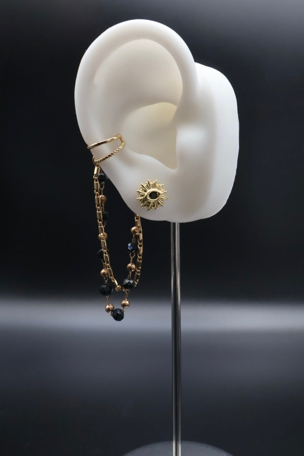 Gold earring on a mannequin ear with a dark background
