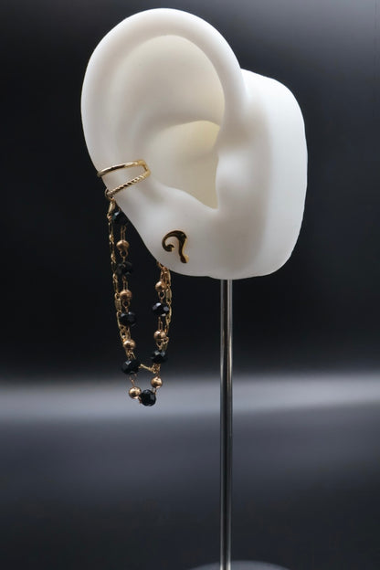 Model of an ear with gold and black earrings on a dark background