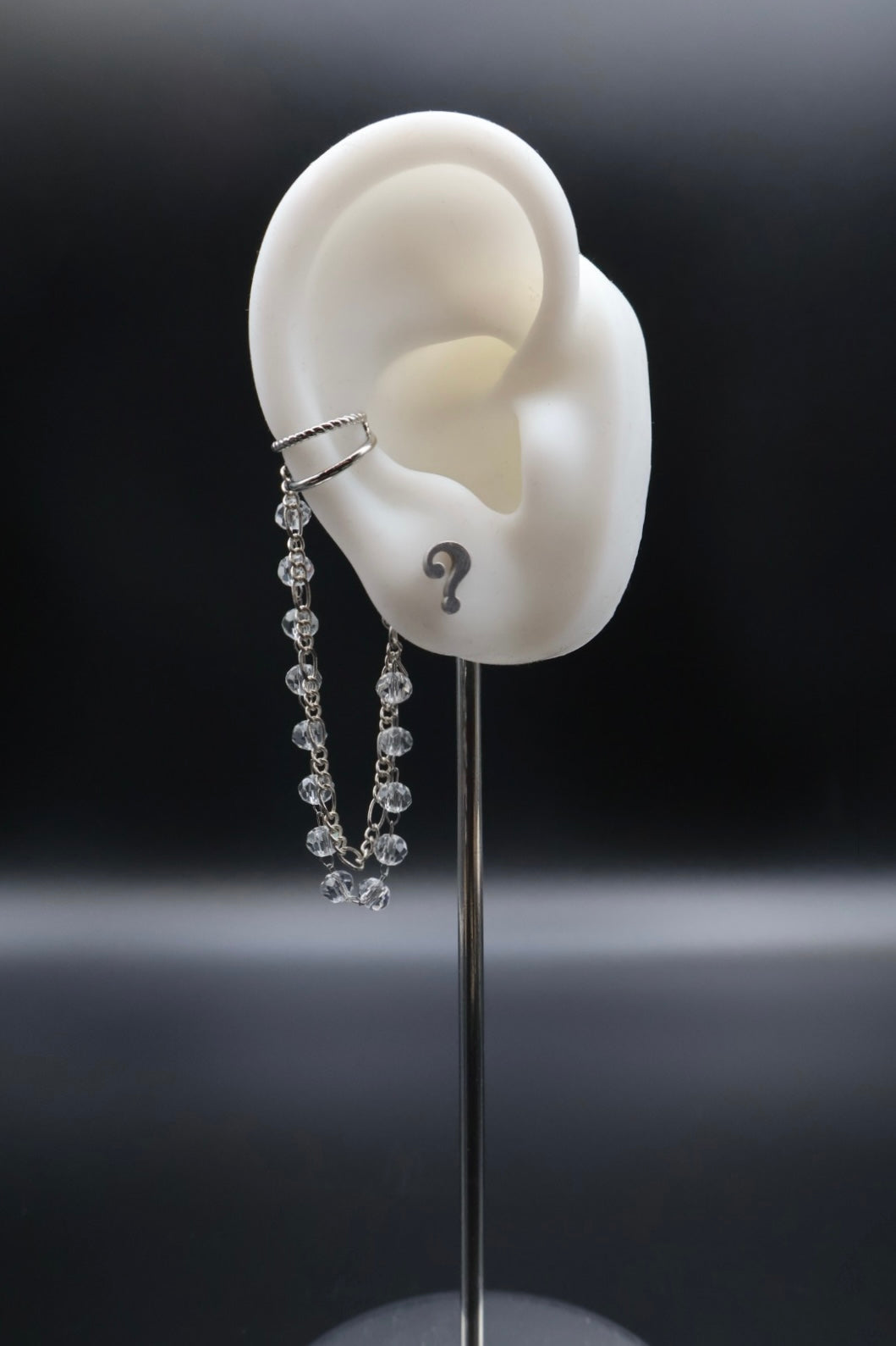 White ear model with a necklace and question mark on a black background
