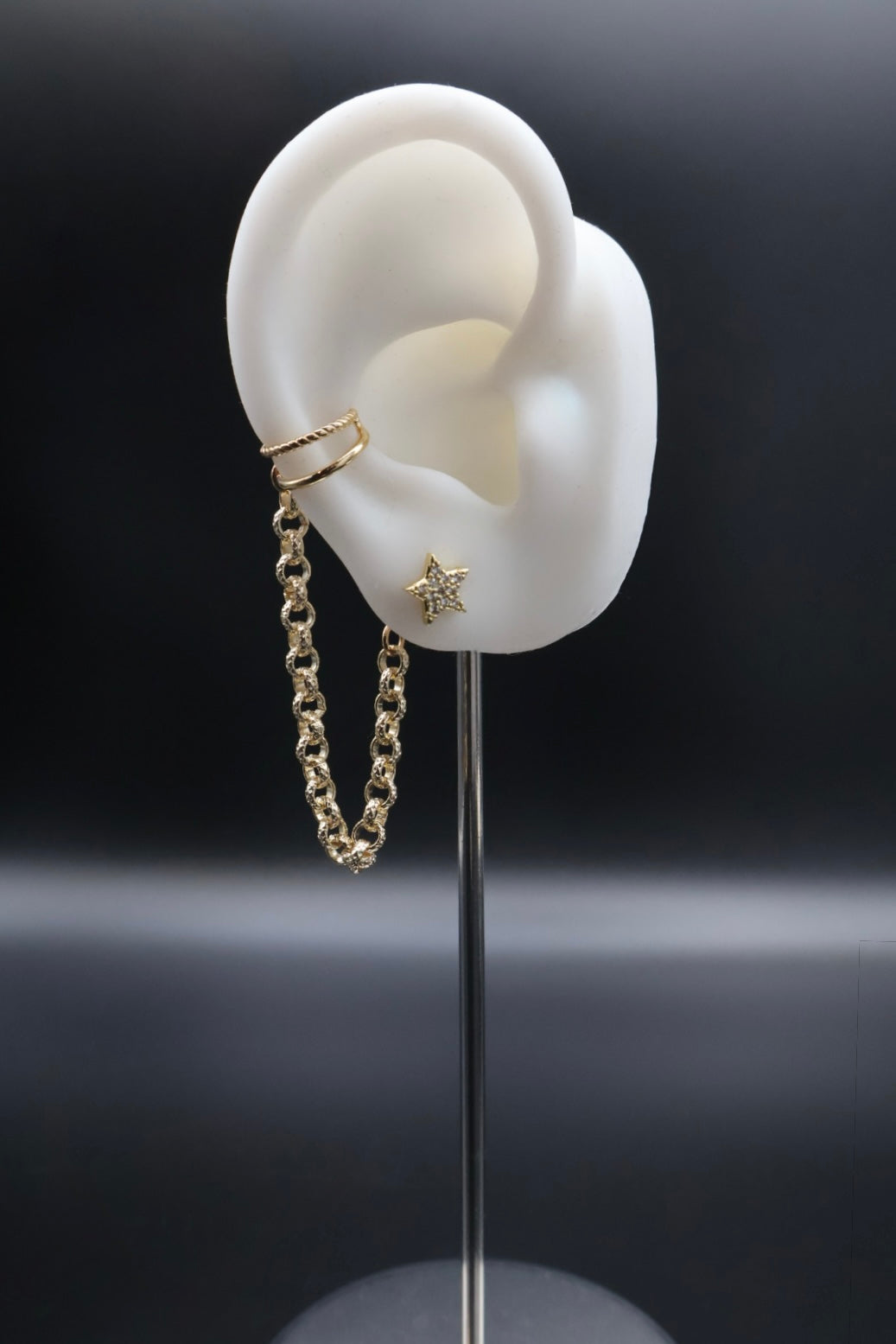 Gold chain earring with star detail on a mannequin ear against a dark background
