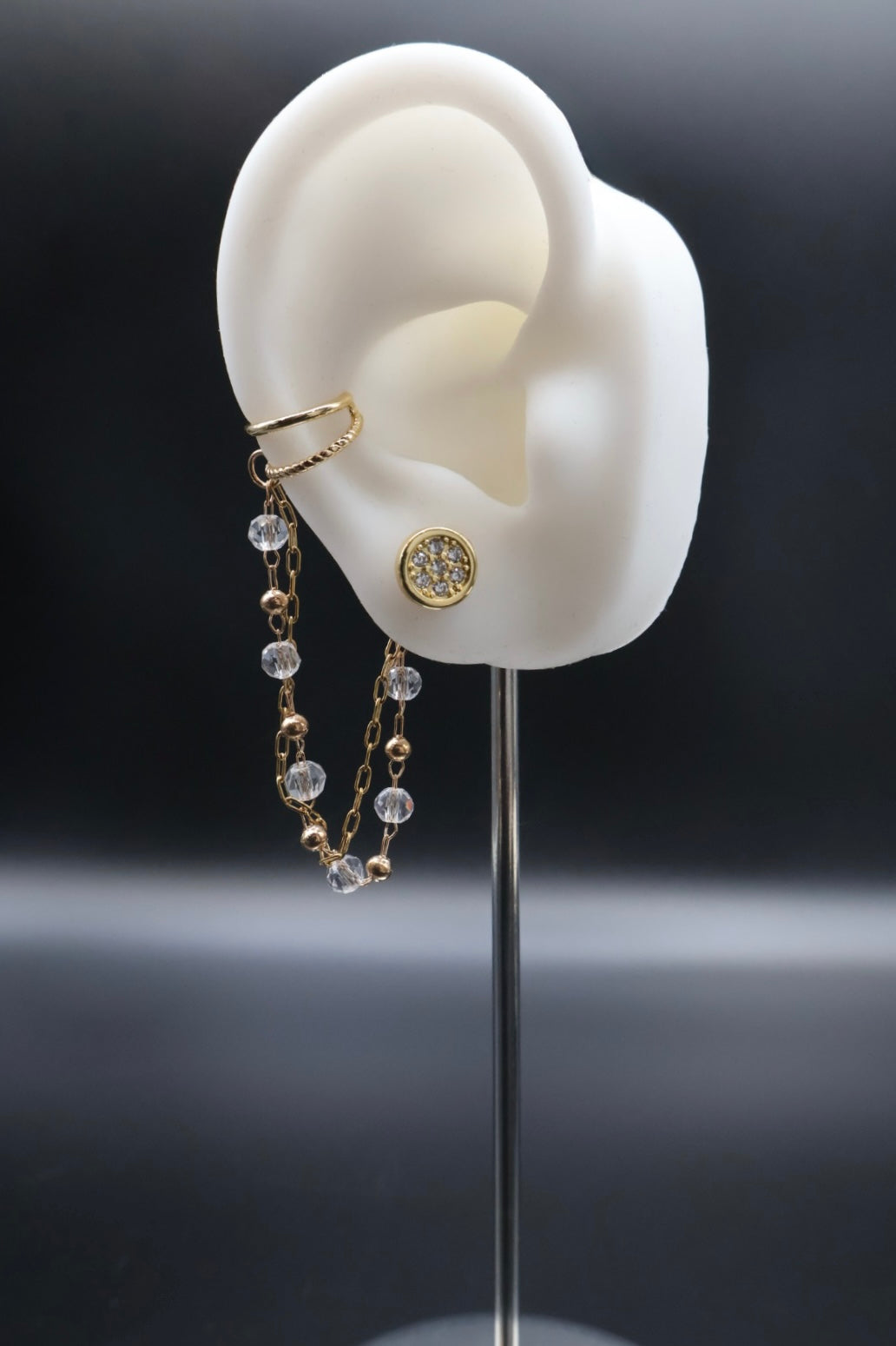 Gold earring on a white ear model with a dark background