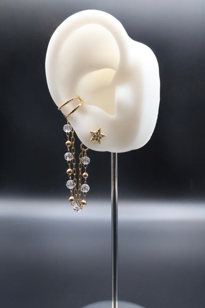 White ear model with gold ring and dangling earrings on a dark background