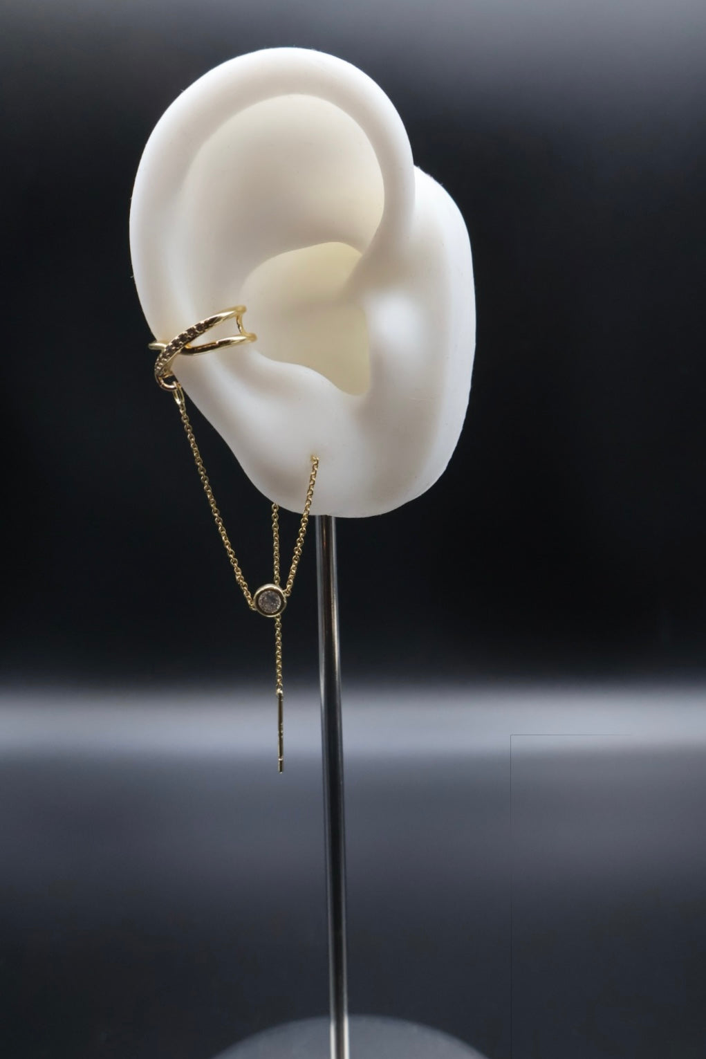 Gold chain earring displayed on a white ear model against a dark background