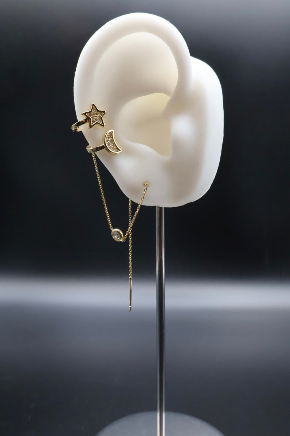 Gold earrings displayed on a white ear model against a dark background
