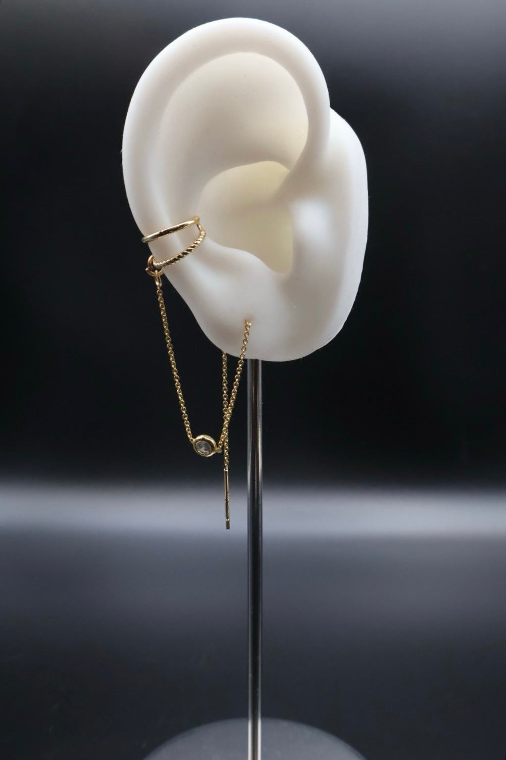 Gold earring displayed on a white ear model against a dark background