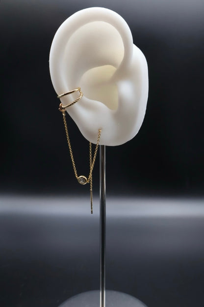Gold earring displayed on a white ear model against a dark background