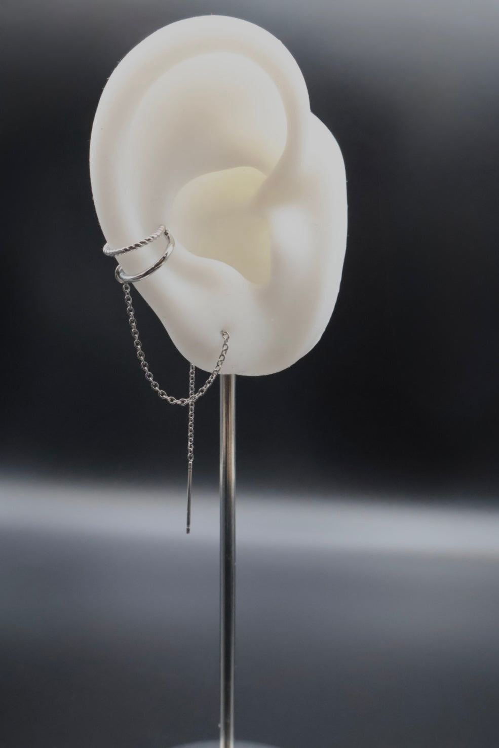 White ear model with a silver earring on a dark background