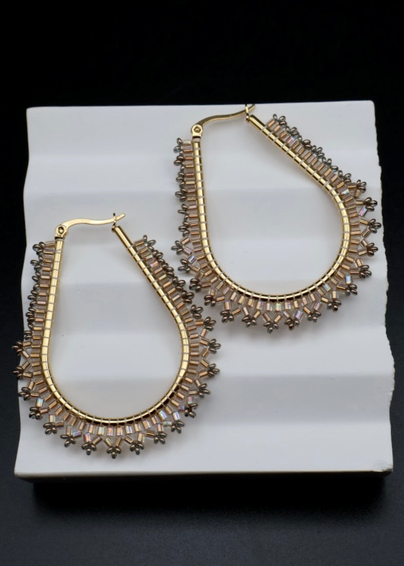 Gold hoop earrings with brown gemstones on a white stand against a black background