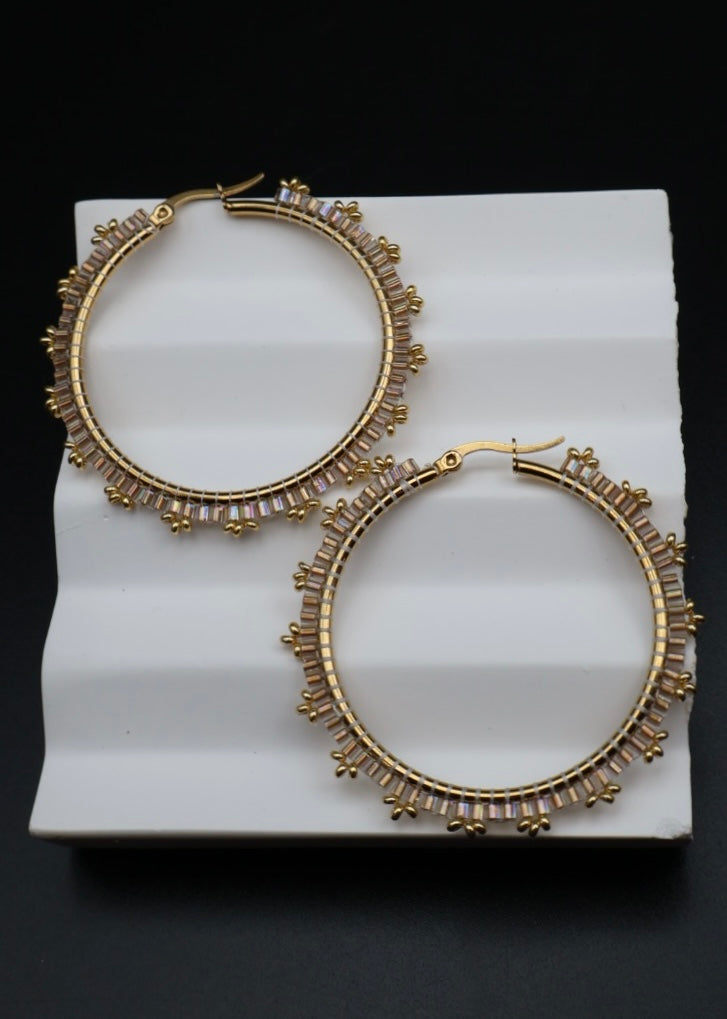 Gold hoop earrings with decorative elements on a white stand against a black background