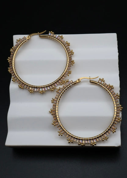 Gold hoop earrings with decorative elements on a white stand against a black background