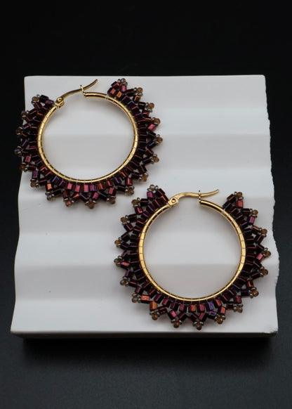 Pair of gold hoop earrings with red gemstones on a white stand against a black background
