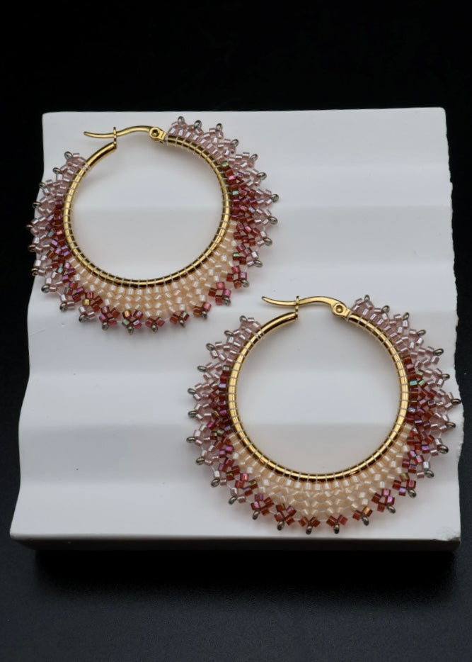 Gold hoop earrings with red gemstones on a white stand against a black background