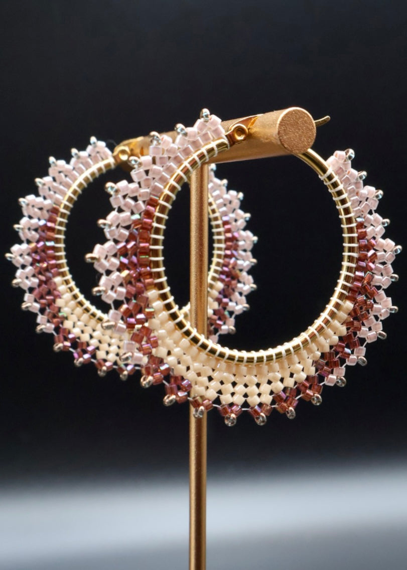 Gold hoop earrings with multicolored gemstones on a stand against a dark background