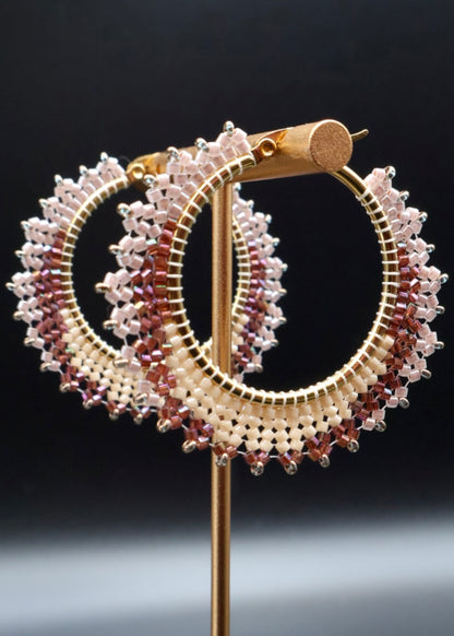 Gold hoop earrings with multicolored gemstones on a stand against a dark background