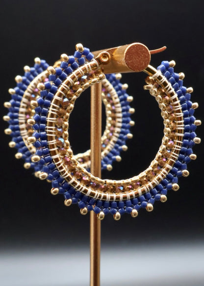 Gold and blue beaded hoop earrings on a stand against a dark background