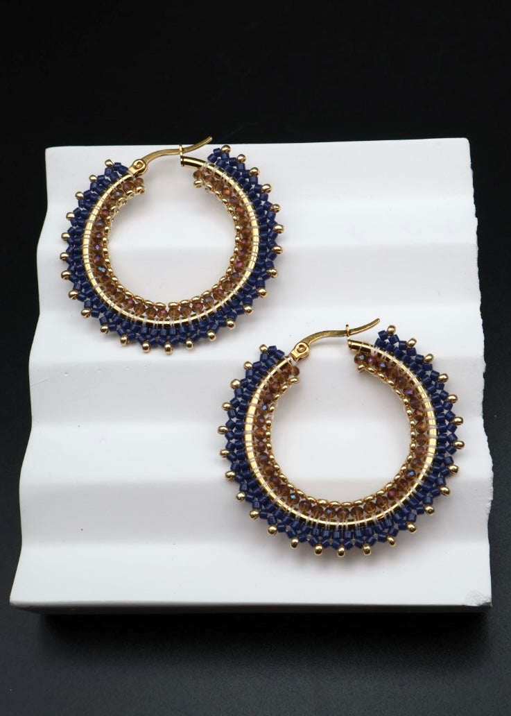 Pair of gold and blue hoop earrings on a white surface with a black background