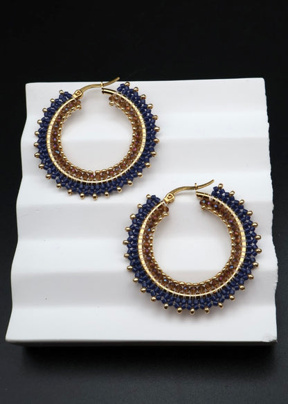 Pair of gold and blue hoop earrings on a white surface with a black background