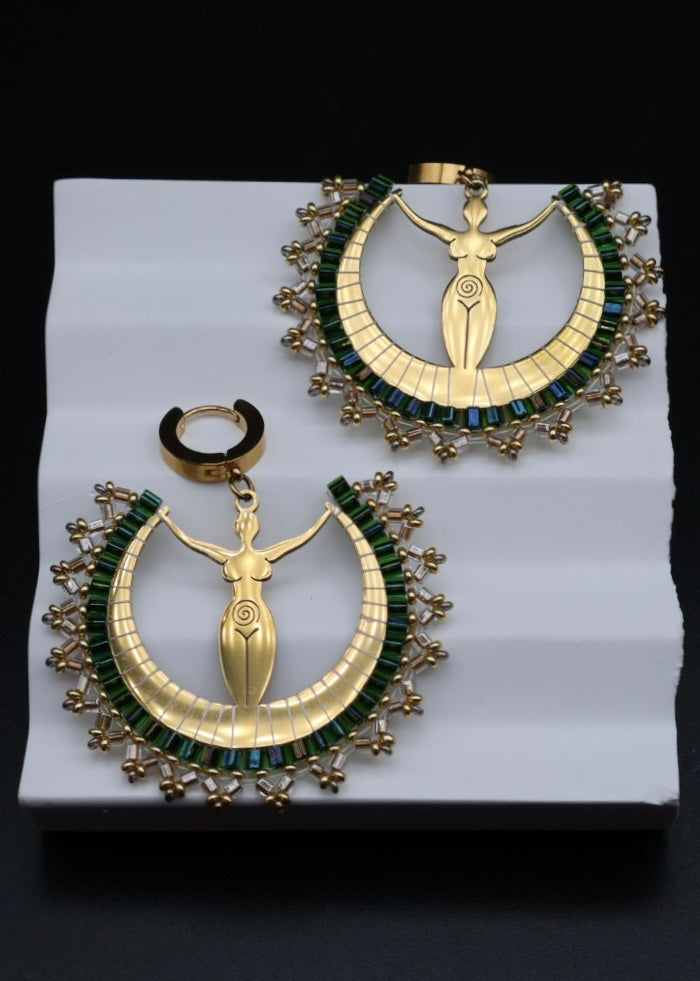 Pair of gold and green earrings on a white stand with a black background