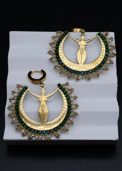 Pair of gold and green earrings on a white stand with a black background