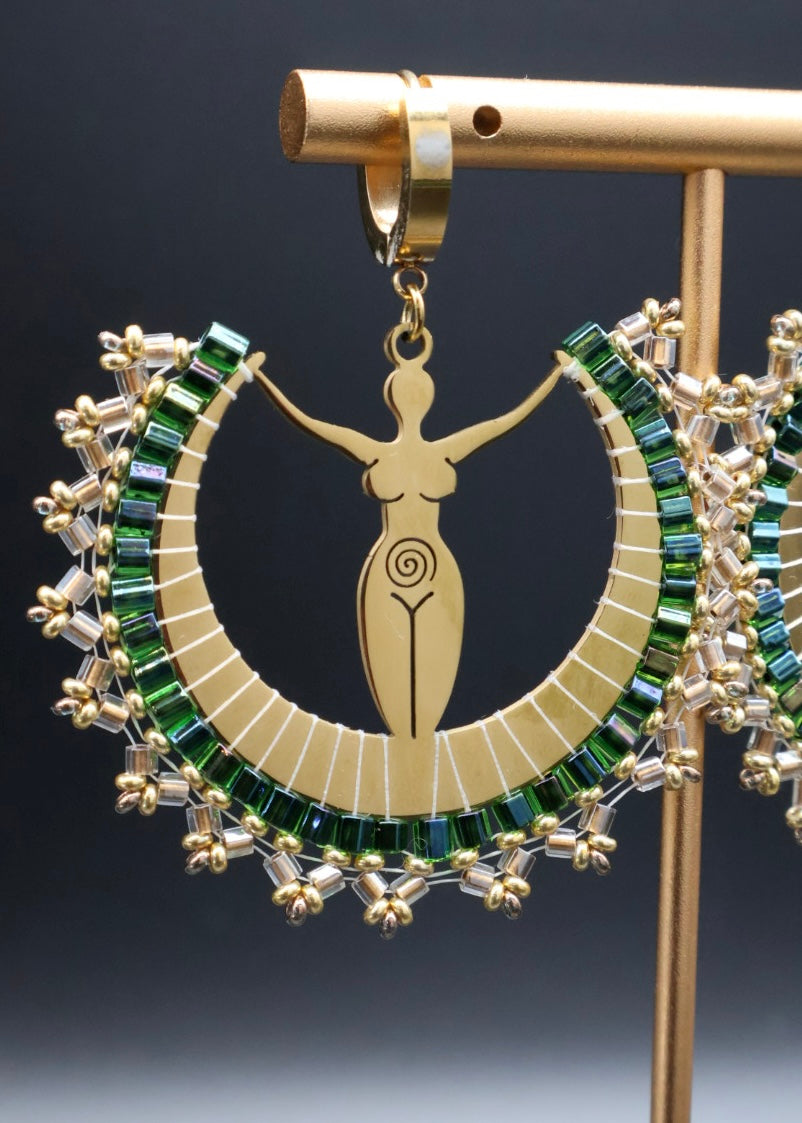 Gold earring with green gemstones on a stand against a dark background