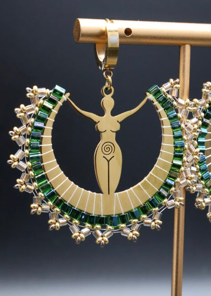 Gold earring with green gemstones on a stand against a dark background
