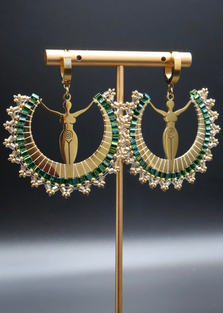 Pair of gold earrings with green gemstones on a stand against a dark background