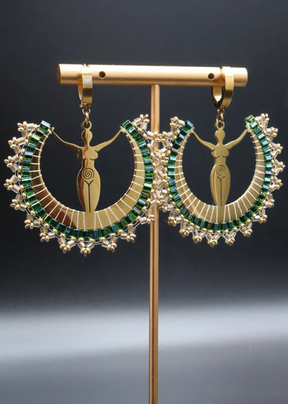 Pair of gold earrings with green gemstones on a stand against a dark background