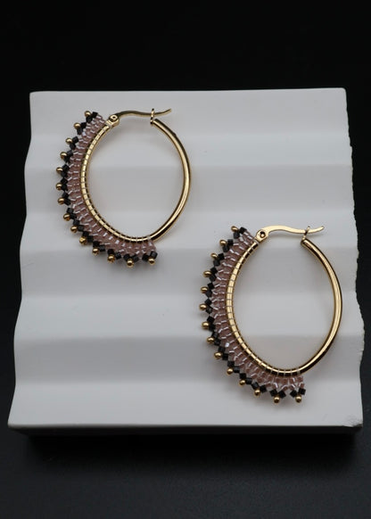 Pair of gold hoop earrings with purple stones on a white stand against a black background