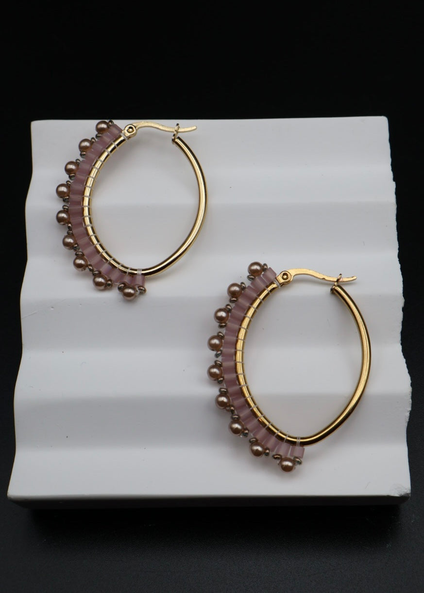 Pair of gold hoop earrings with purple beads on a white stand against a black background