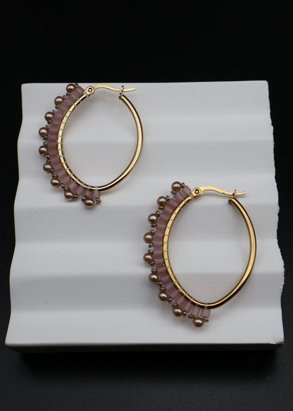 Pair of gold hoop earrings with purple beads on a white stand against a black background