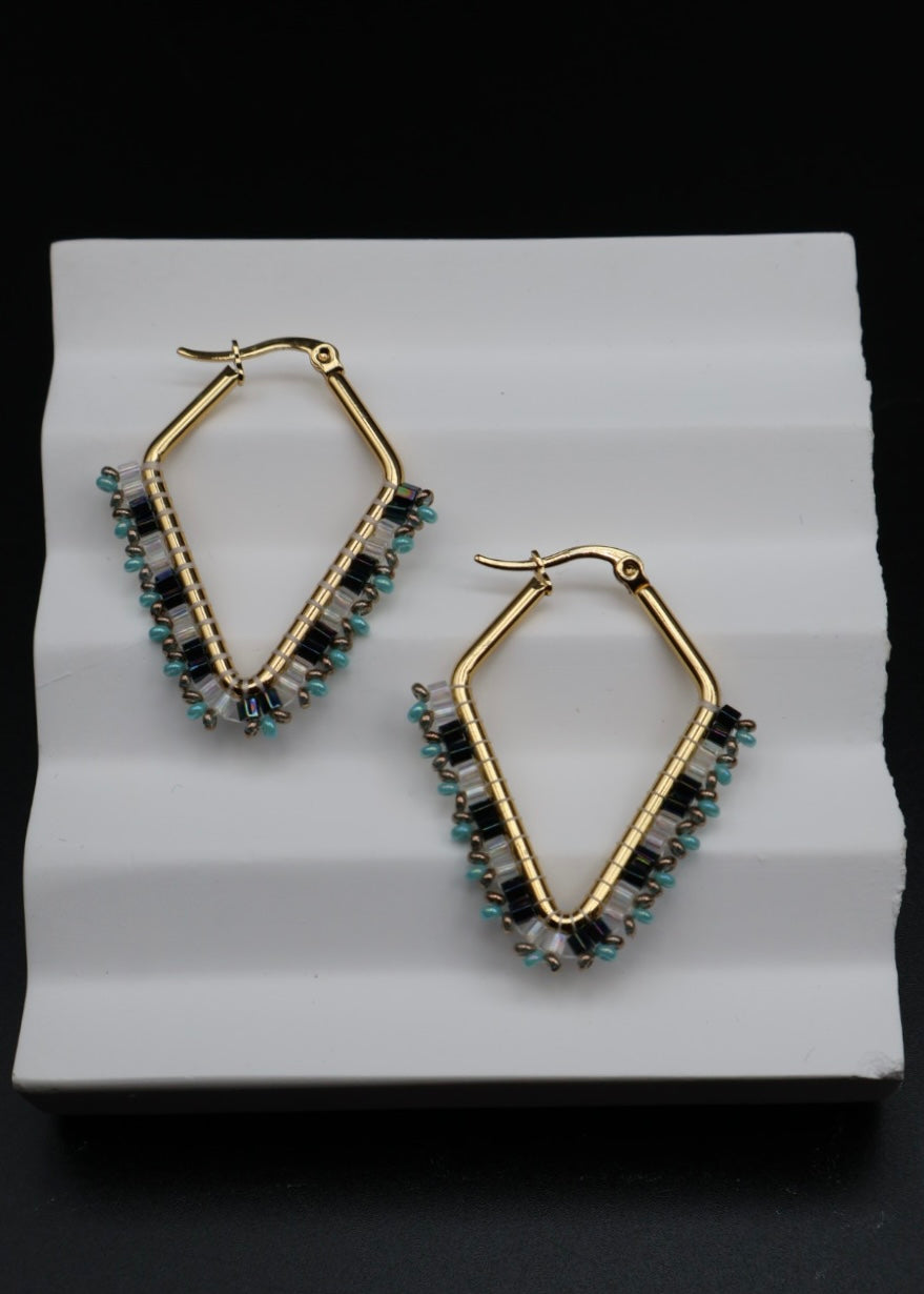 Gold hoop earrings with gemstones on a white stand against a black background