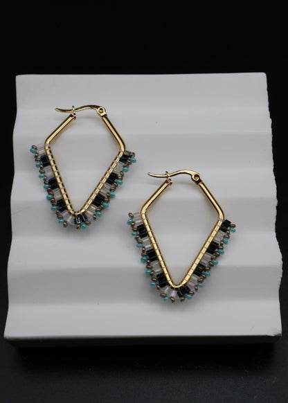 Gold hoop earrings with gemstones on a white stand against a black background