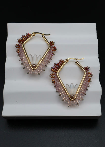 Pair of gold-framed hoop earrings with bead detailing on a white stand.
