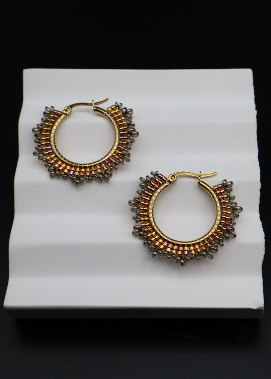 Pair of gold hoop earrings with brown gemstones on a white stand.