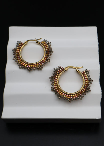 Pair of gold hoop earrings with brown gemstones on a white stand.