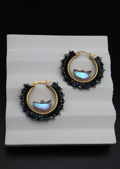 Gold hoop earrings with gemstone accents on a white card against a black background