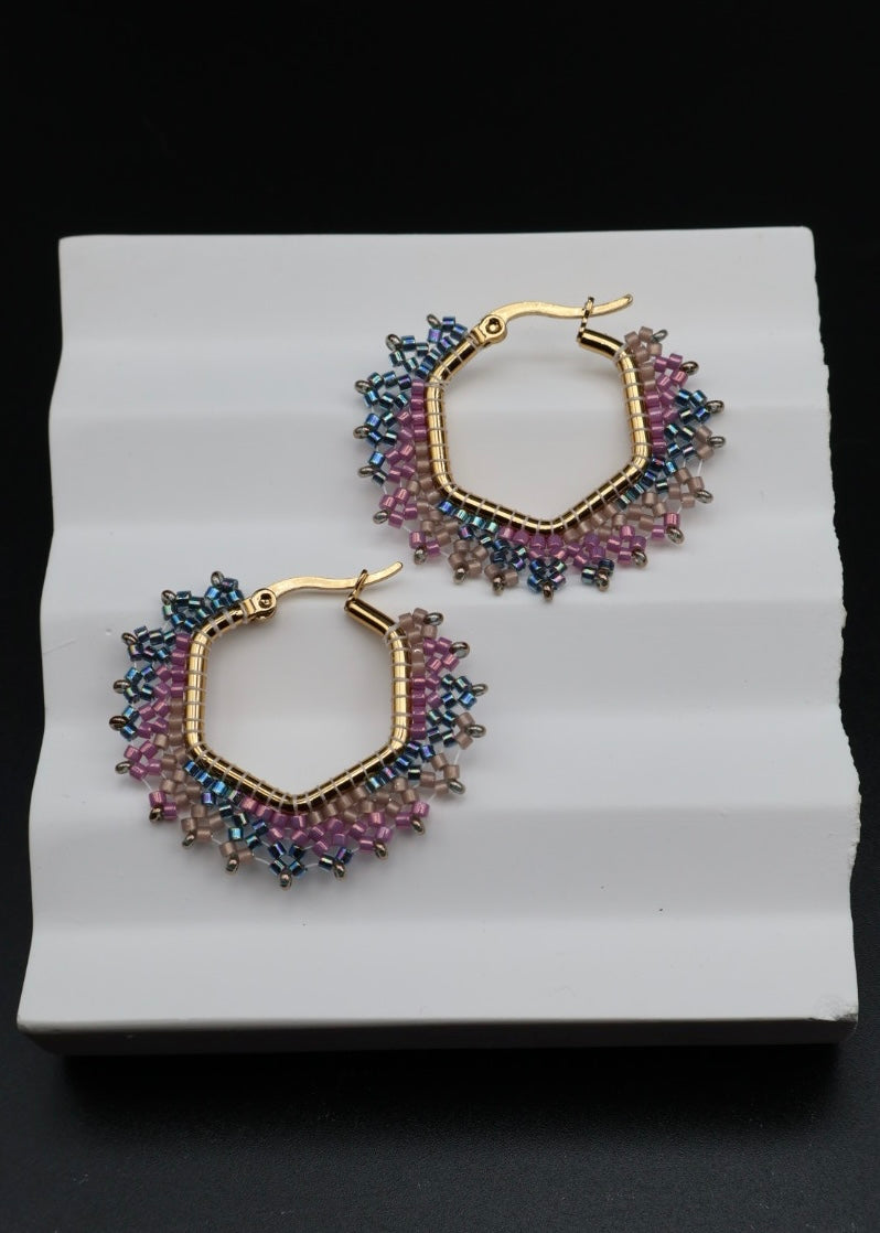 Pair of gold hoop earrings with colorful beads on a white stand against a black background