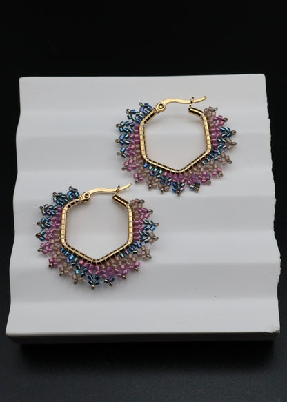 Pair of gold hoop earrings with colorful beads on a white stand against a black background