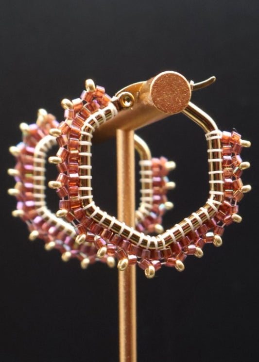 Gold hoop earrings with pink gemstones on a black background