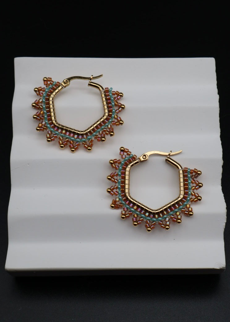 Pair of gold hoop earrings with intricate designs on a white stand against a black background