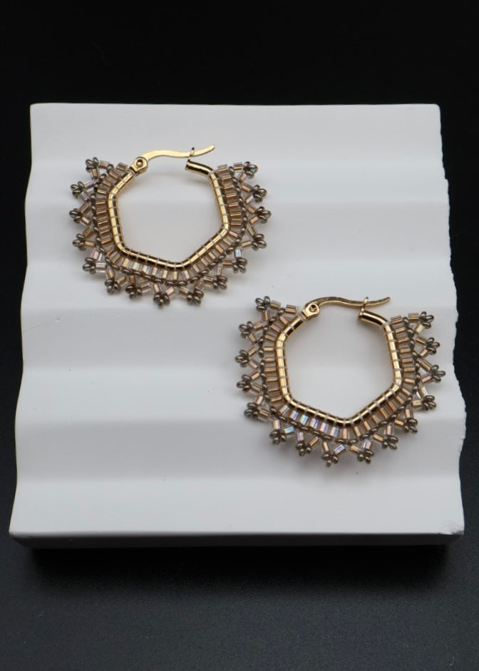 Gold hoop earrings with gemstone accents on a white stand against a black background
