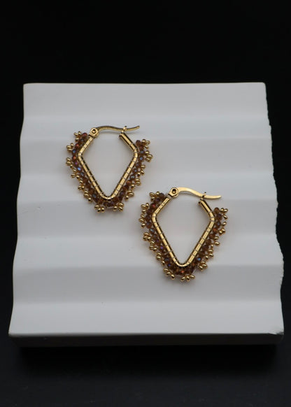 Gold hoop earrings on a white stand with a black background