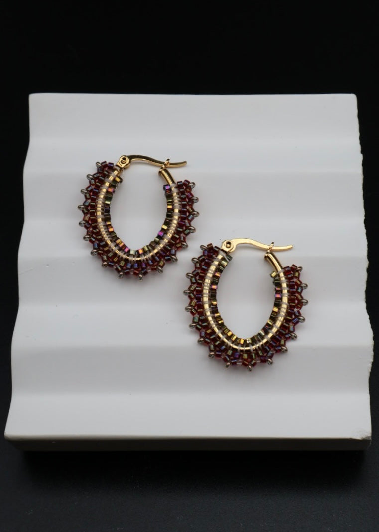 Pair of gold hoop earrings with red beads on a white stand against a black background