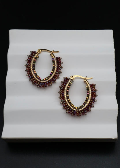 Pair of gold hoop earrings with red beads on a white stand against a black background