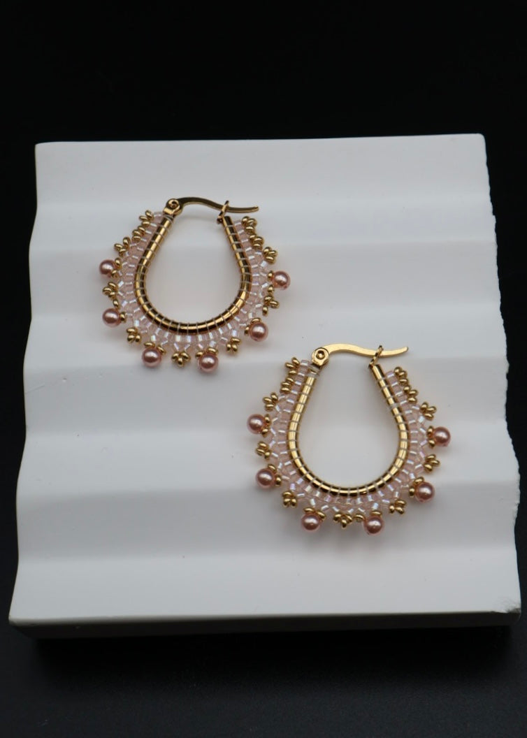 Gold hoop earrings with pink beads on a white stand against a black background