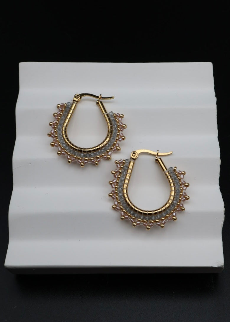 Gold hoop earrings on a white stand with a black background