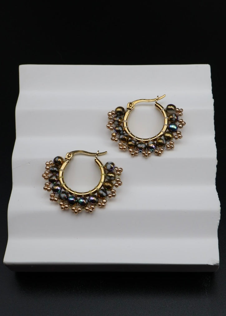 Gold hoop earrings with black beads on a white stand against a black background